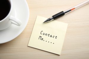 A yellow sticky note is written something on the desk with a cup of coffee and a ball pen aside.